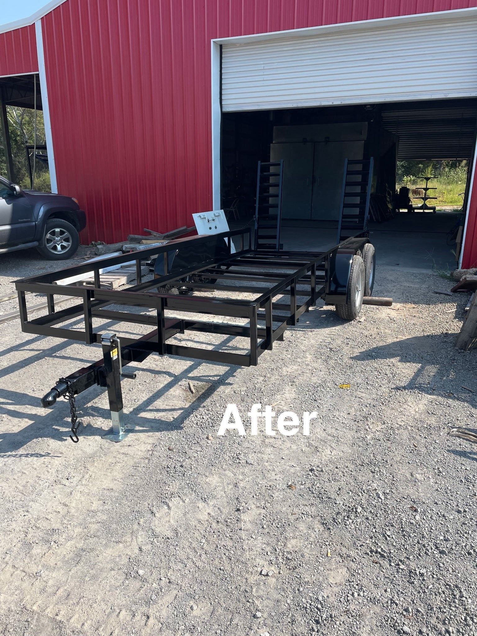 Black trailer in front of a red barn with a white open garage door.
