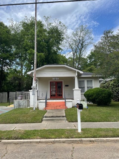 A one-story white house with a red front door, a front porch with columns, a concrete walkway, and a mailbox.