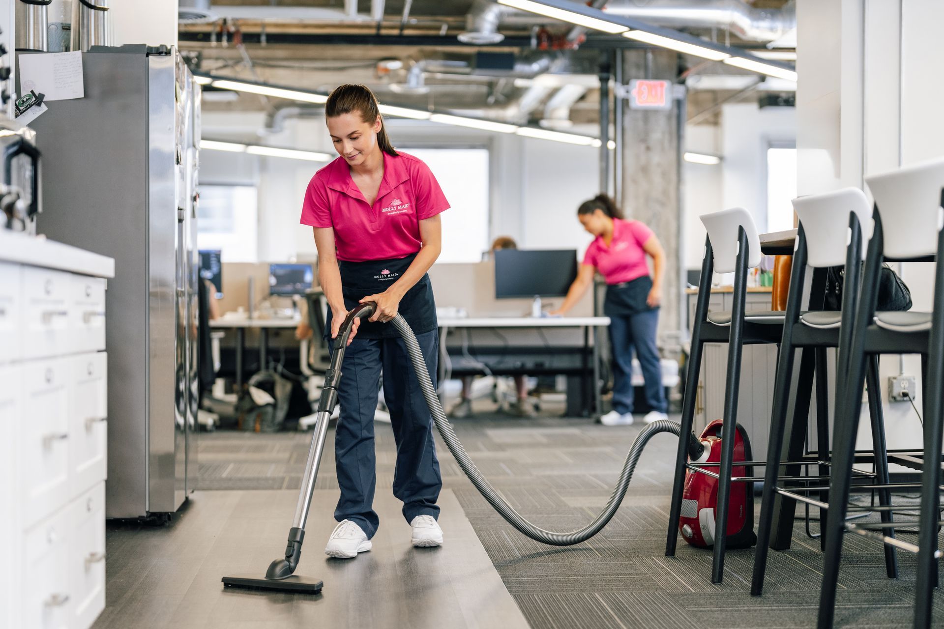 A woman is cleaning the floor of an office with a vacuum cleaner.
