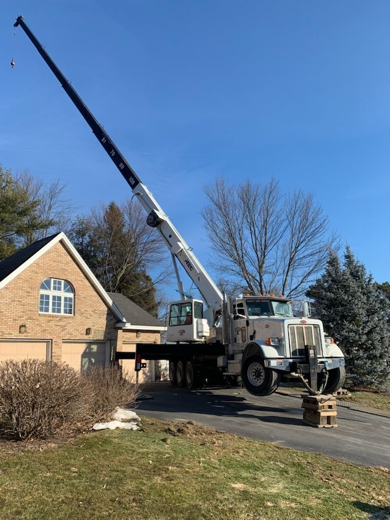 Crane with raised boom in front of a house on a driveway, under a clear blue sky.