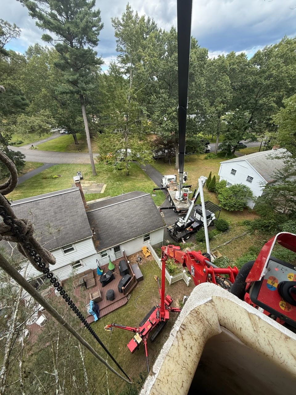 A crane over a yard with a house and trees; a red piece of machinery sits below.