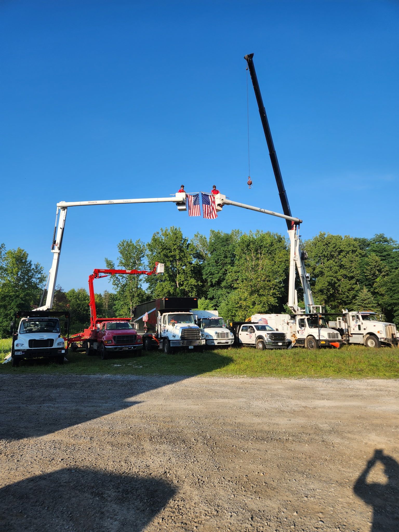Several utility trucks supporting a large arch with an American flag; clear blue sky backdrop.