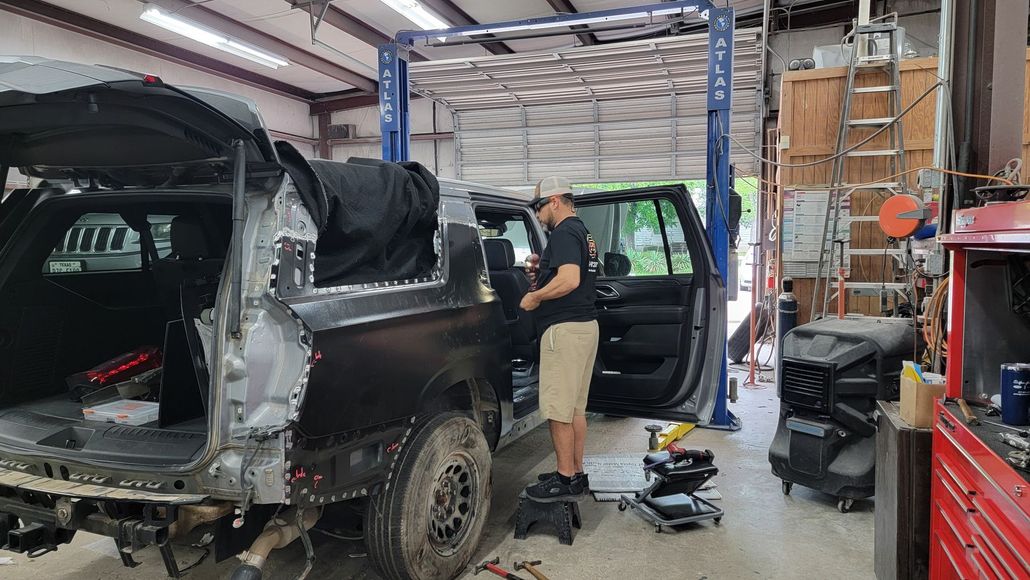 Worker repairing a black SUV in an auto shop, with tools and parts scattered nearby.