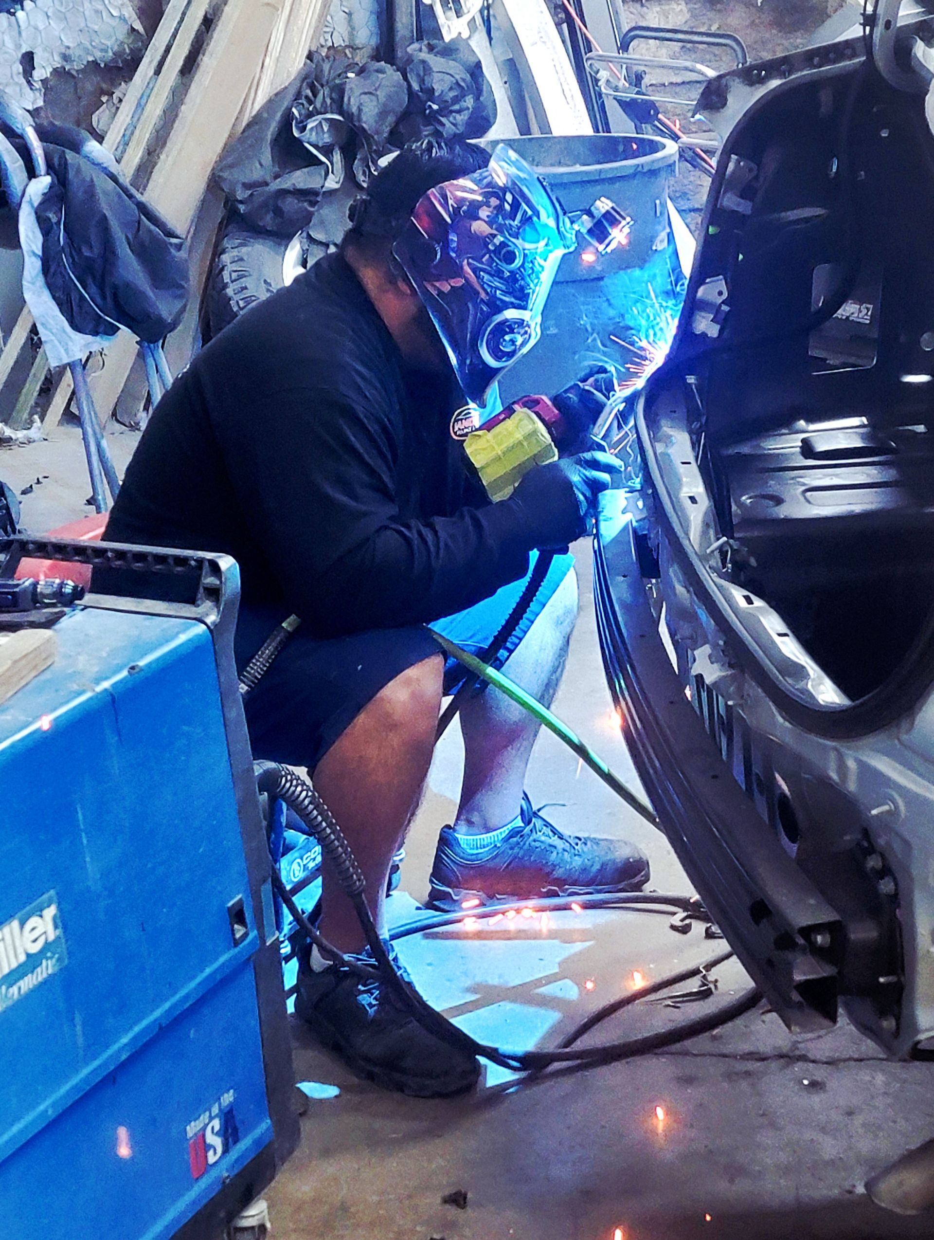 Person welding inside a car frame, bright blue sparks in a garage.