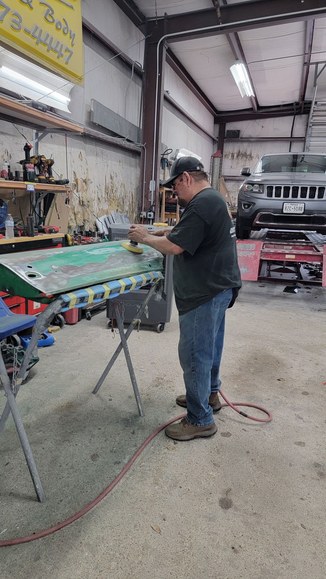 Person working on a painted car panel in a garage workshop, with tools and a vehicle in the background