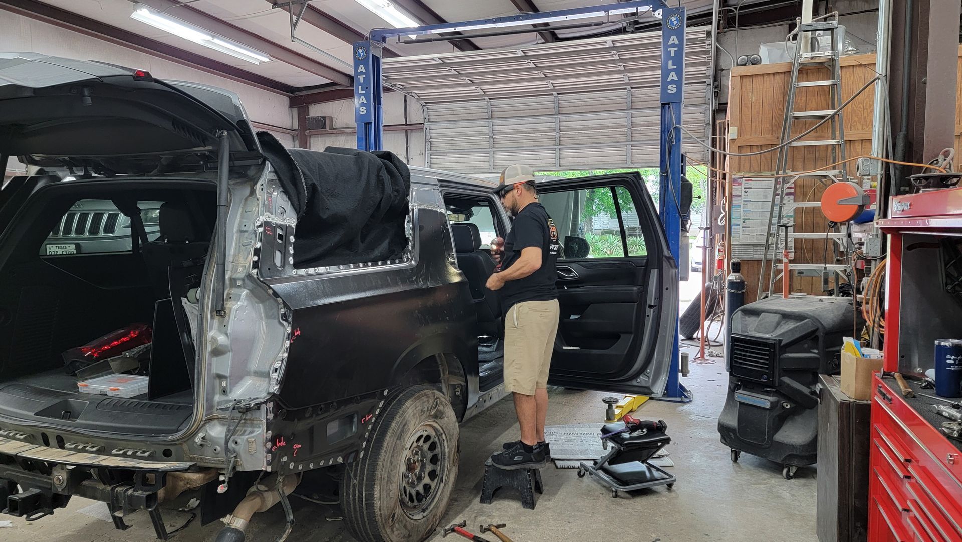 Mechanic working on a black SUV in a garage, with tools and parts scattered around.