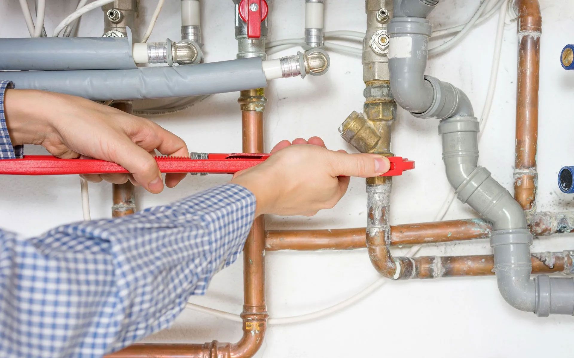 Plumber measuring and aligning gray and copper pipes with a red level in a utility area