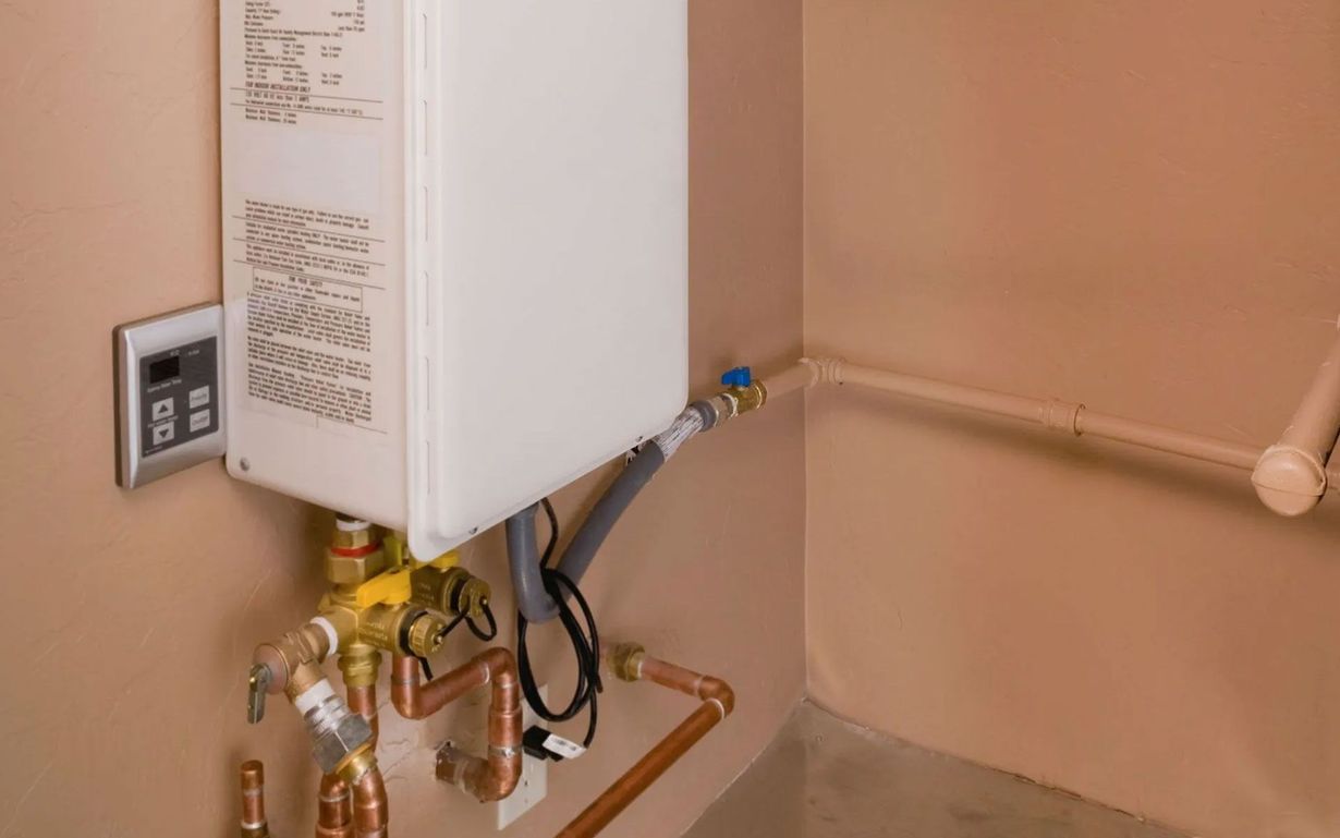 A wall-mounted tankless water heater with copper piping and a digital control panel, set against a plain beige wall.
