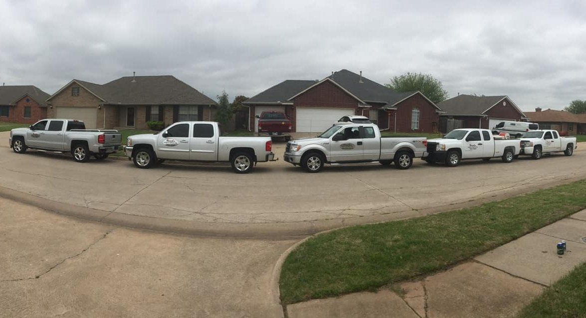 Six trucks parked on a curved street in front of houses under cloudy skies, possibly indicating a pest control or maintenance operation