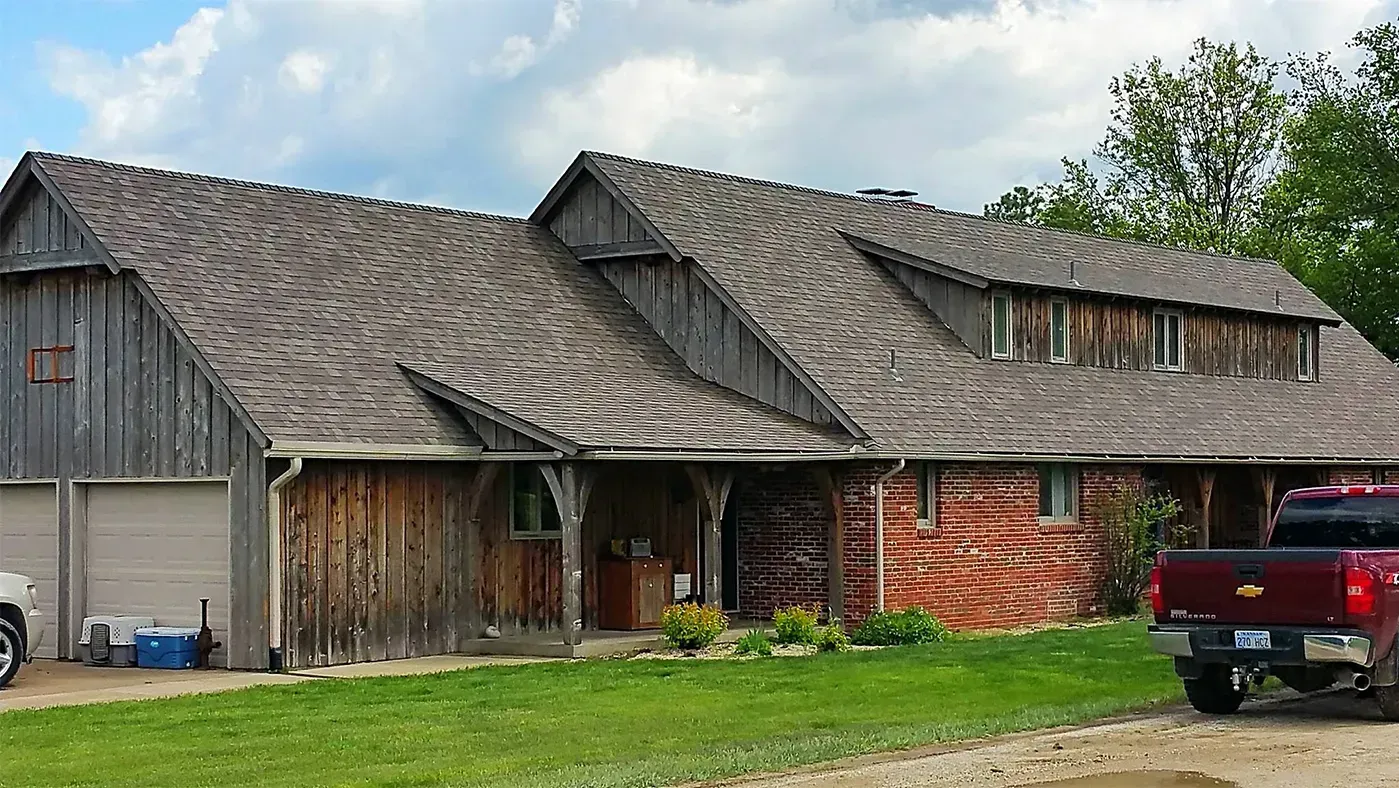 A single-story rustic building with a dark wood exterior, shingled roof, a garage, and a red pickup truck parked in front.