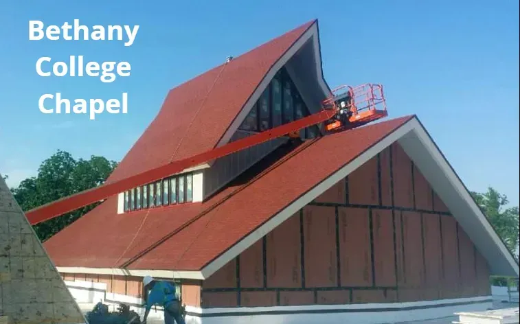 An aerial view of the Bethany College Chapel with a red roof, being repaired by a worker in an orange aerial lift.