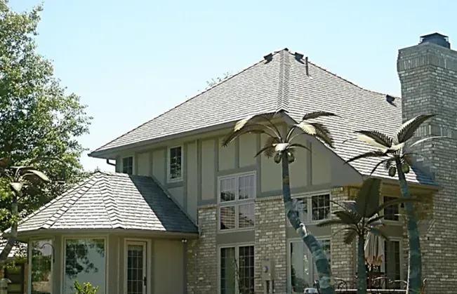 A two-story house with stone siding, a gray roof, and decorative palm tree sculptures in the front yard.