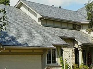 A multi-level suburban home with grey shingled roofing, light-colored siding, and a partial view of a garage and entryway.