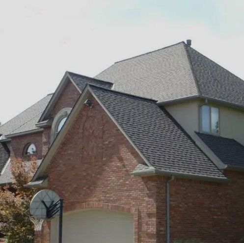 An angled view of a house with a red brick garage, light-colored walls, and dark gray shingled roofs.