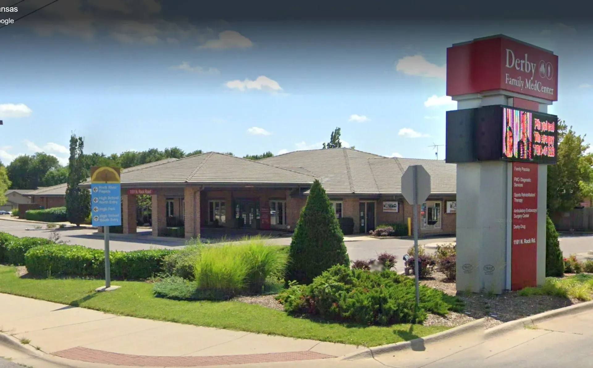 A tan building with a wide driveway and a red-topped sign for Derby Family Medicine in a bright, sunny landscape.