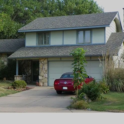 A two-story suburban home with a light-colored facade, stone accents, and a red car parked in the driveway.
