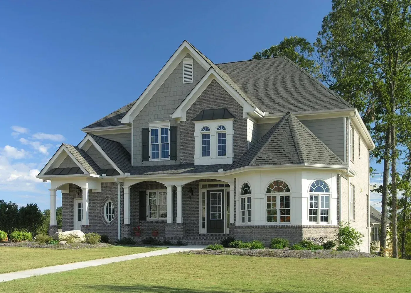 Two-story gray brick house with white trim, a covered front porch, and a turret-style room on the right.