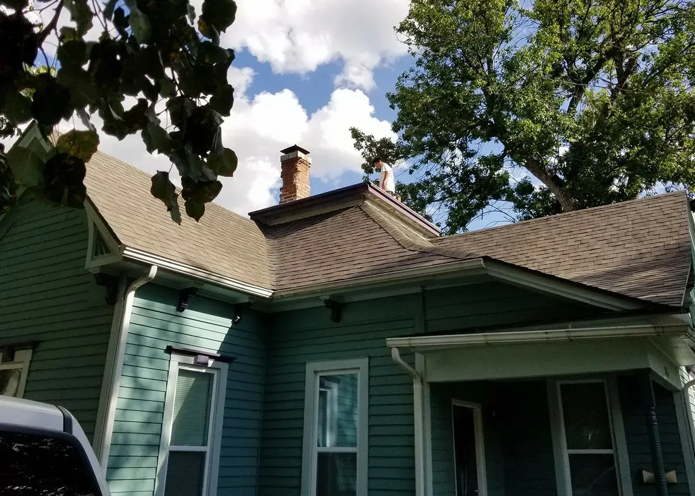 A teal-colored house with a dark shingled roof and a brick chimney under a partly cloudy sky.