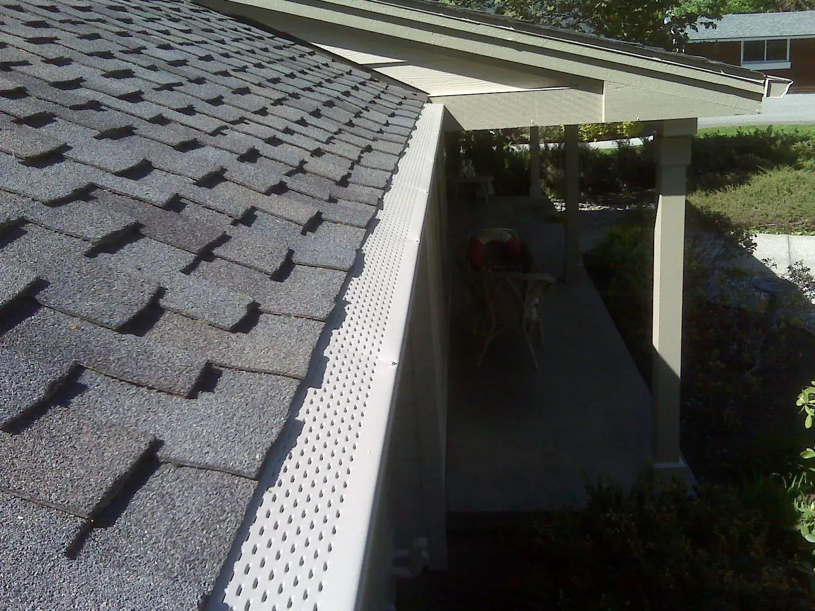 A close-up view of a shingled roof edge with a white gutter guard installed over the rain gutter along a home's porch.