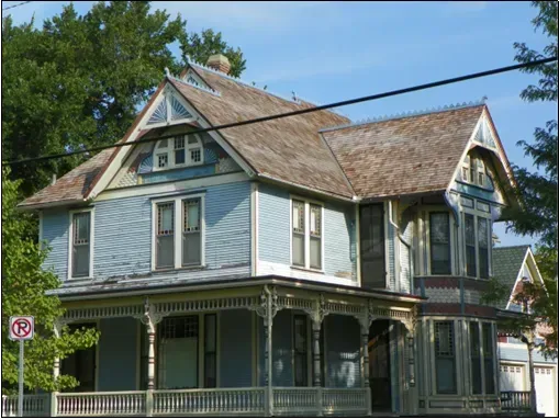 A blue, two-story Victorian-style house with intricate wood trim, a wrap-around porch, and a shingled roof.