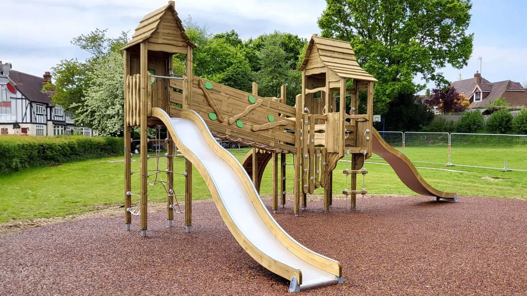 Wooden playground structure with slides on a grassy park field