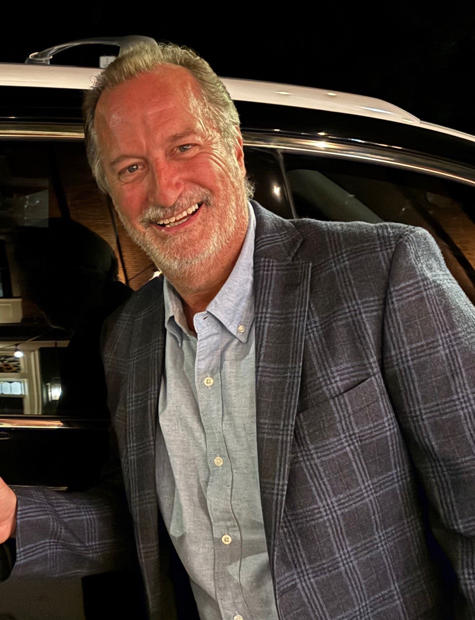 A man in a suit is standing in front of a car.