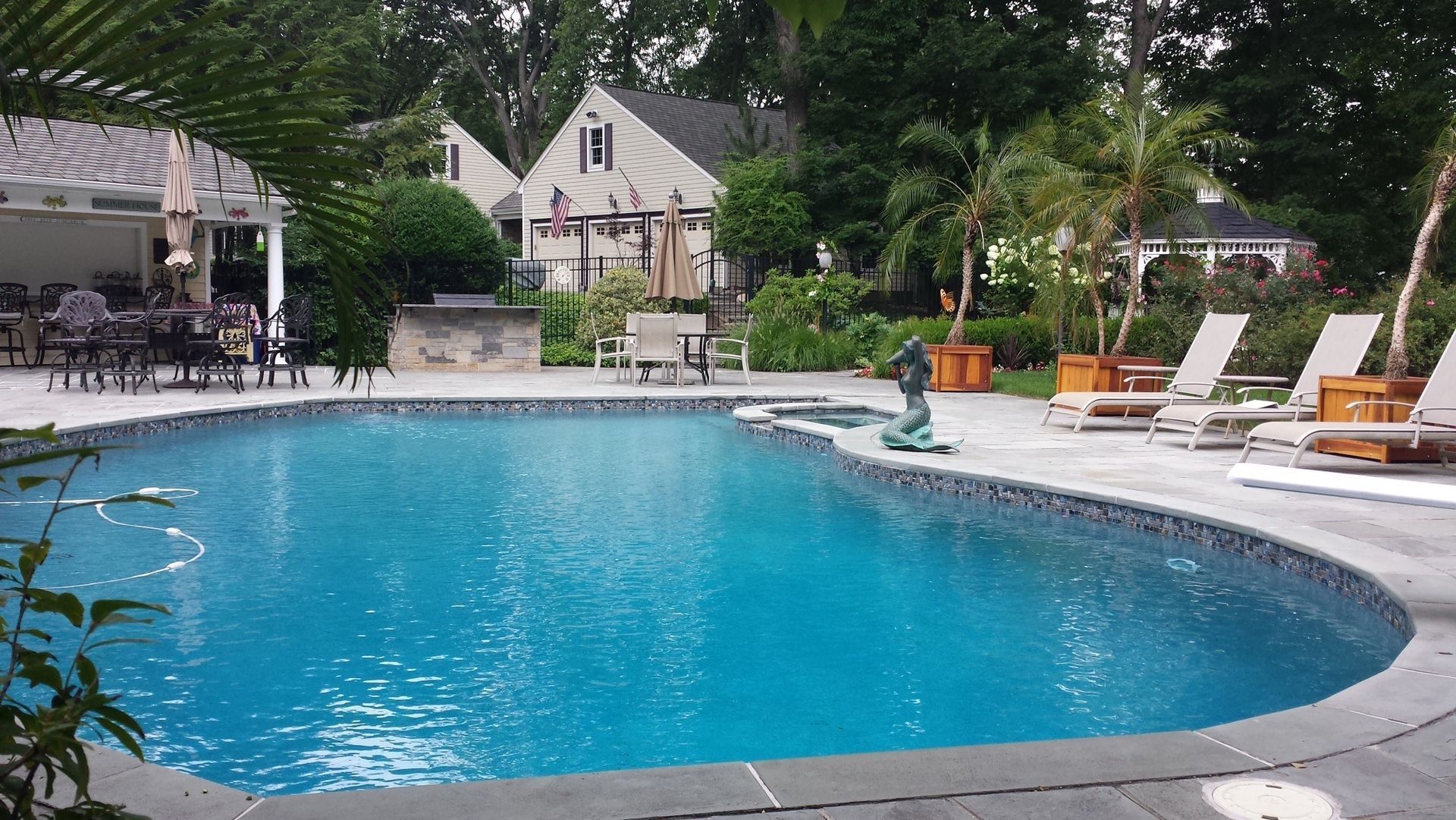 A large swimming pool surrounded by chairs and umbrellas in a backyard.
