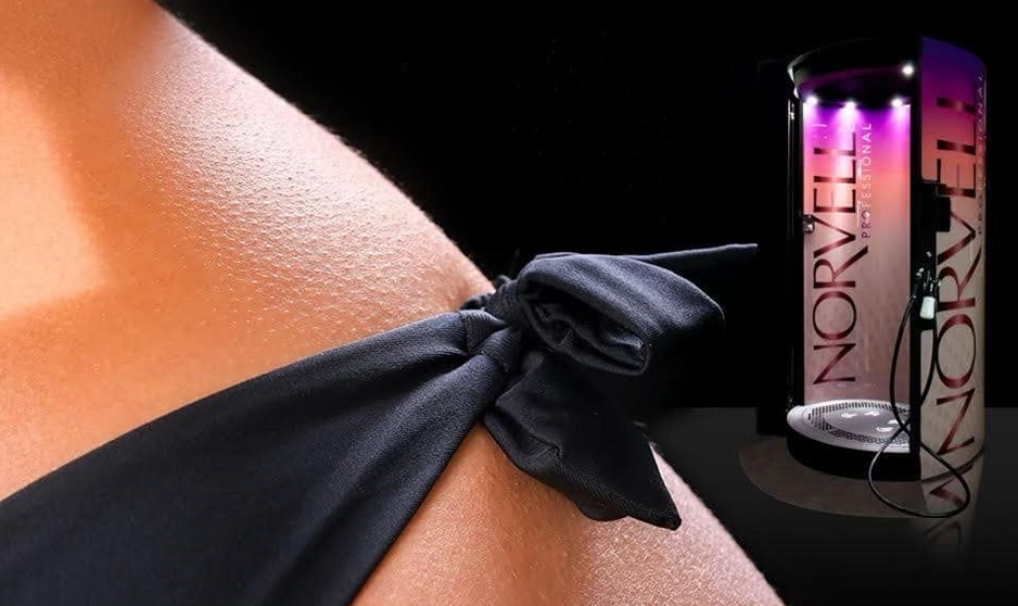 A woman's arm is tied with a black bow next to a Norvell tanning booth.