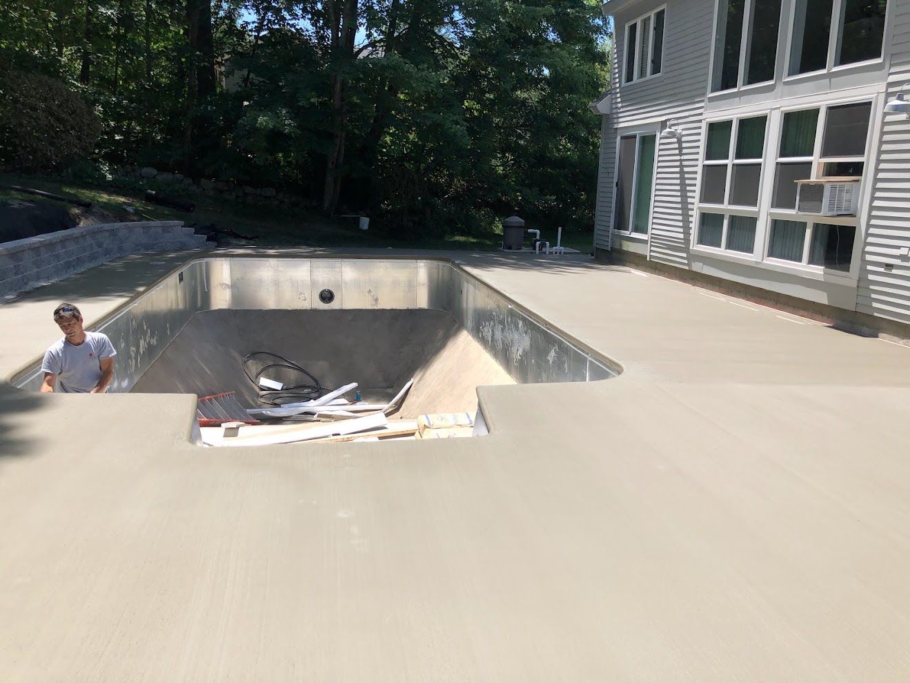 A man is standing on top of a concrete patio next to a swimming pool.