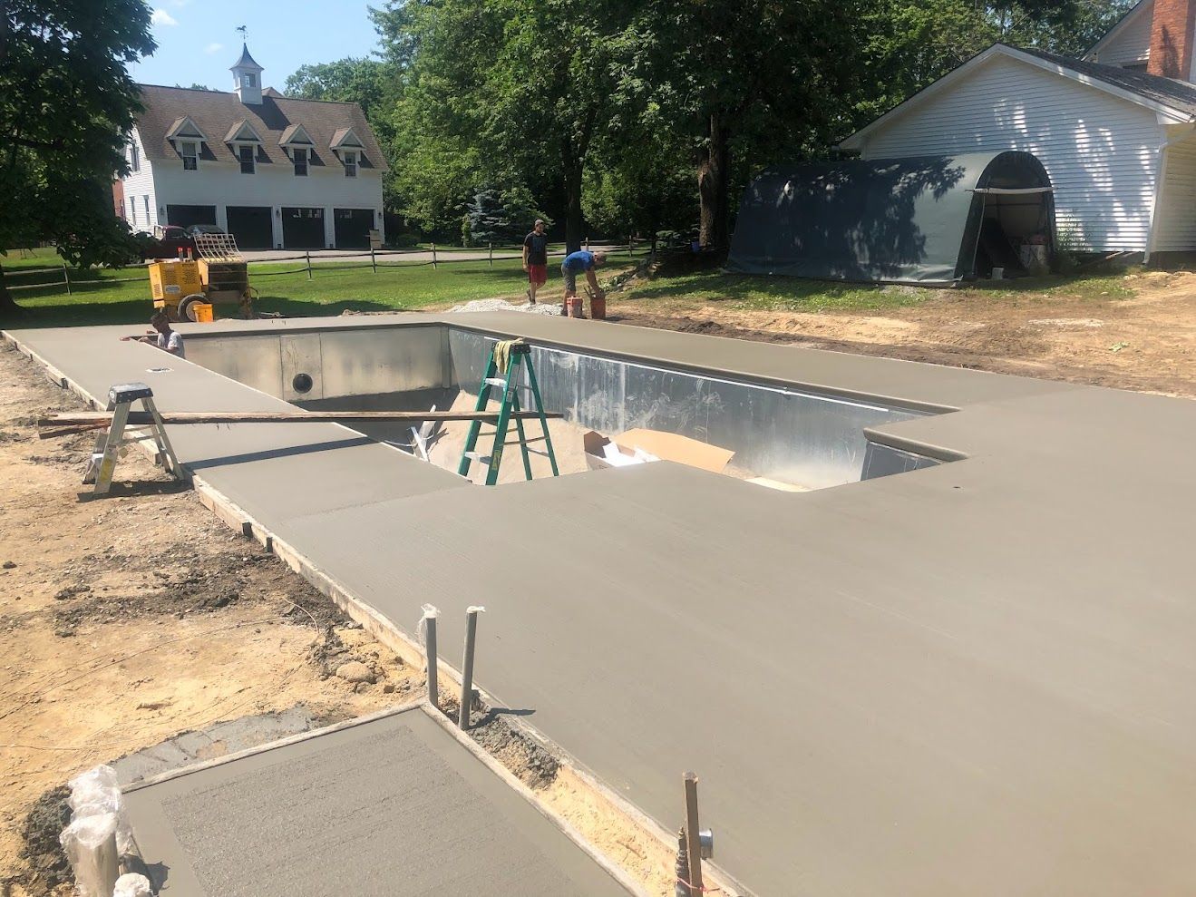 A concrete driveway is being built around a swimming pool.
