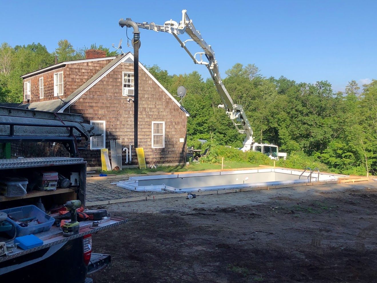 A concrete pump is being used to pour concrete into a pool in front of a house.