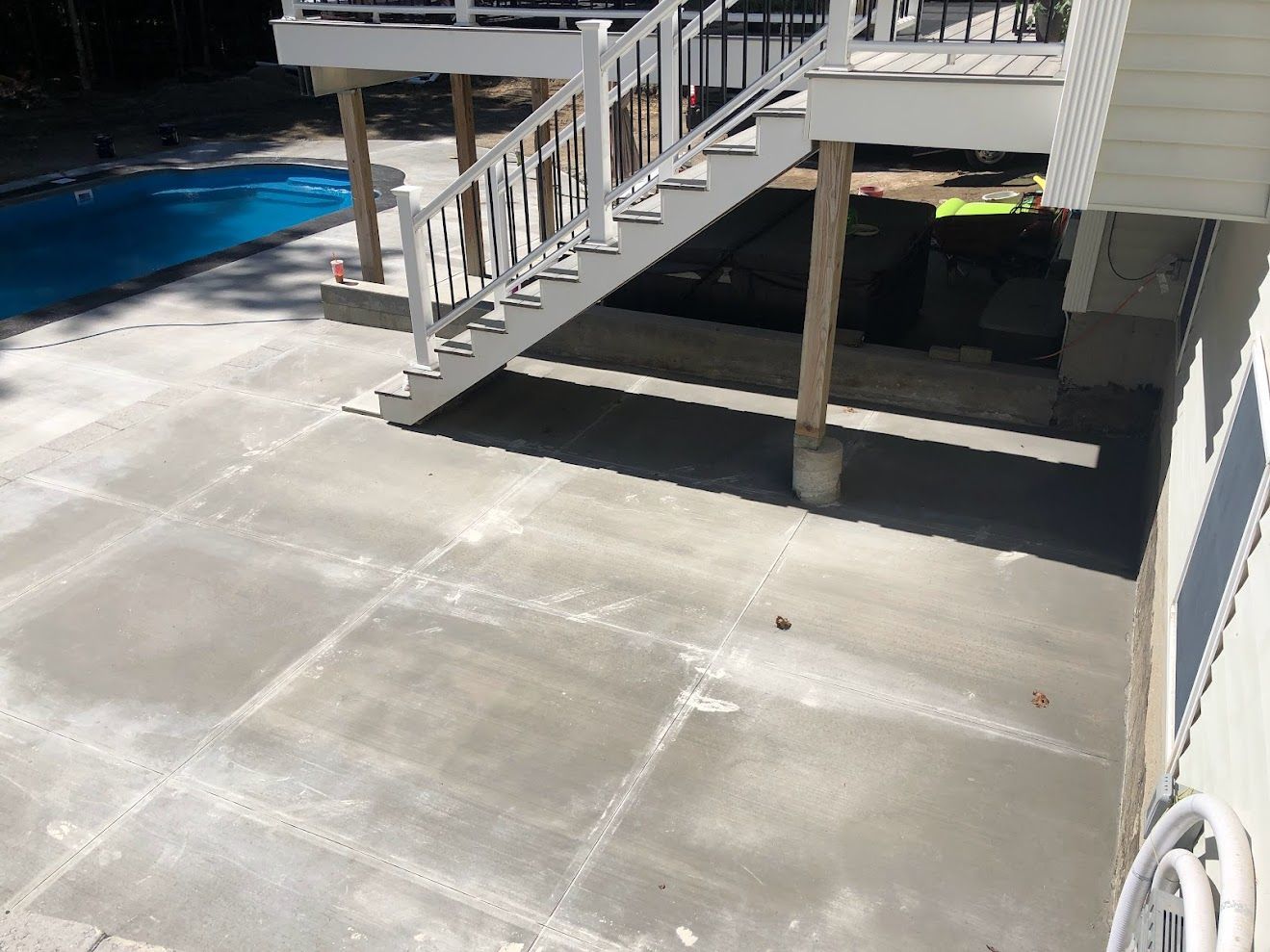 A concrete patio with stairs leading up to a deck next to a pool.