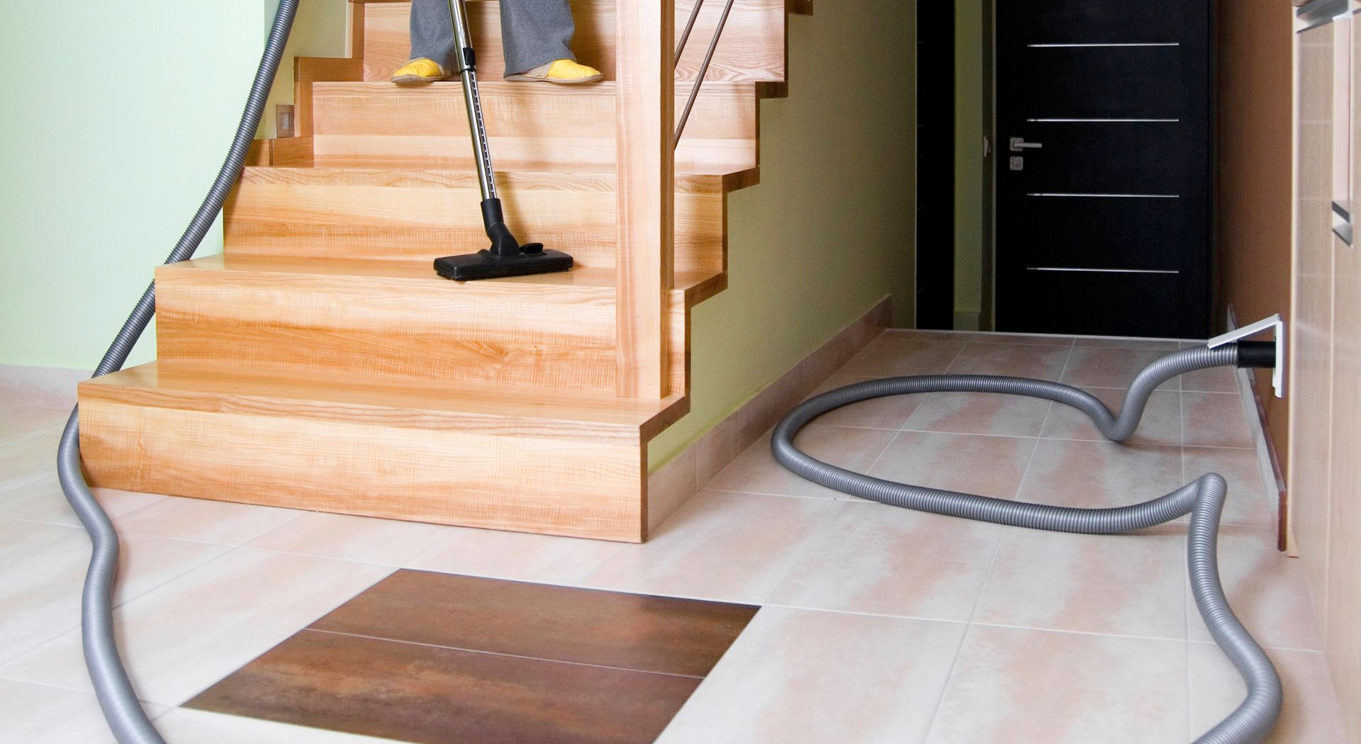 Person vacuuming wooden stairs with a hose connected to a wall outlet.