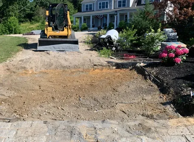 A bulldozer is moving dirt in a driveway in front of a house