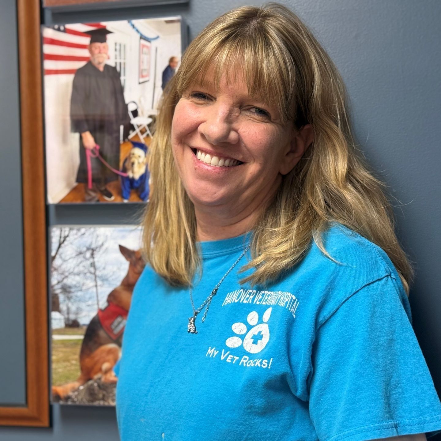 Woman in blue shirt smiles, with photos of a graduate and a dog in the background.
