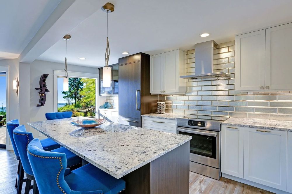 Modern kitchen with white cabinets, granite countertops, blue bar stools, and a view.