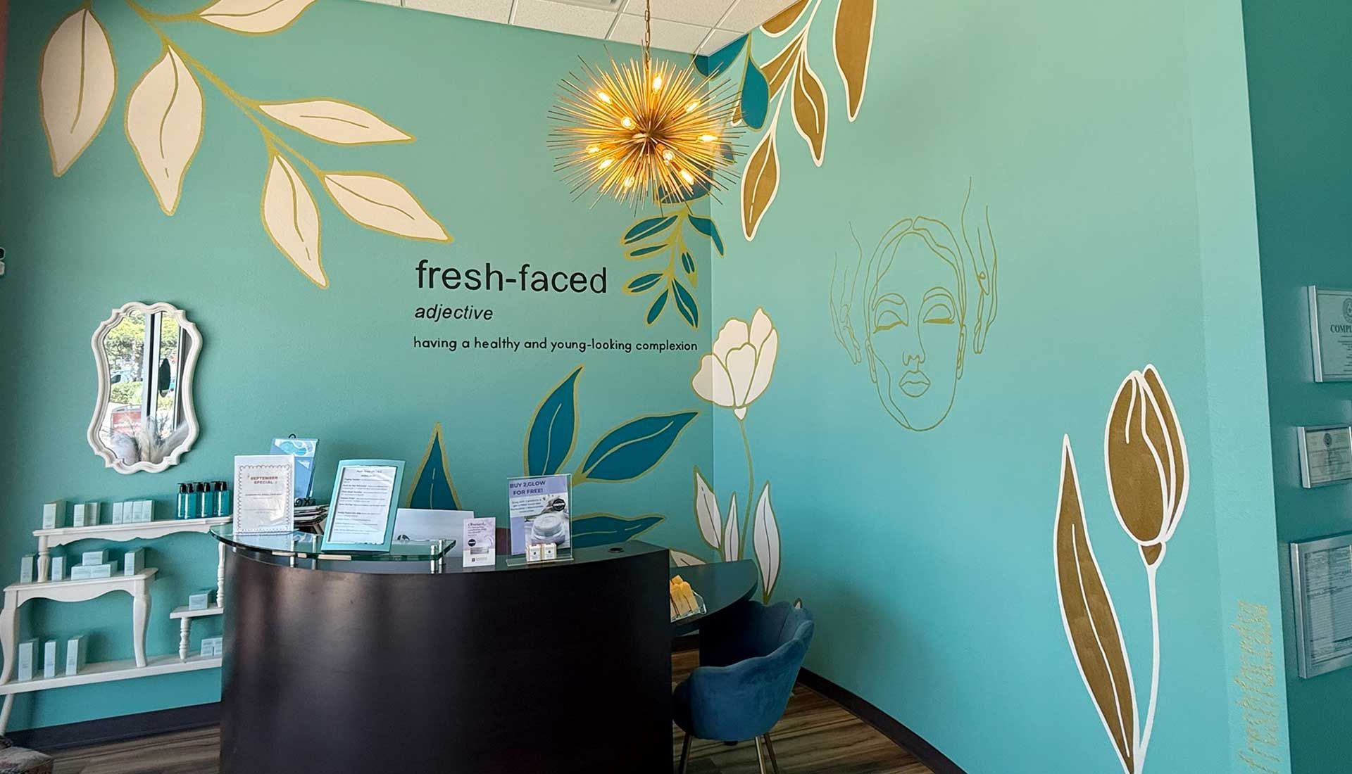 A spa reception area with a teal wall, gold leaf art, and a black desk.