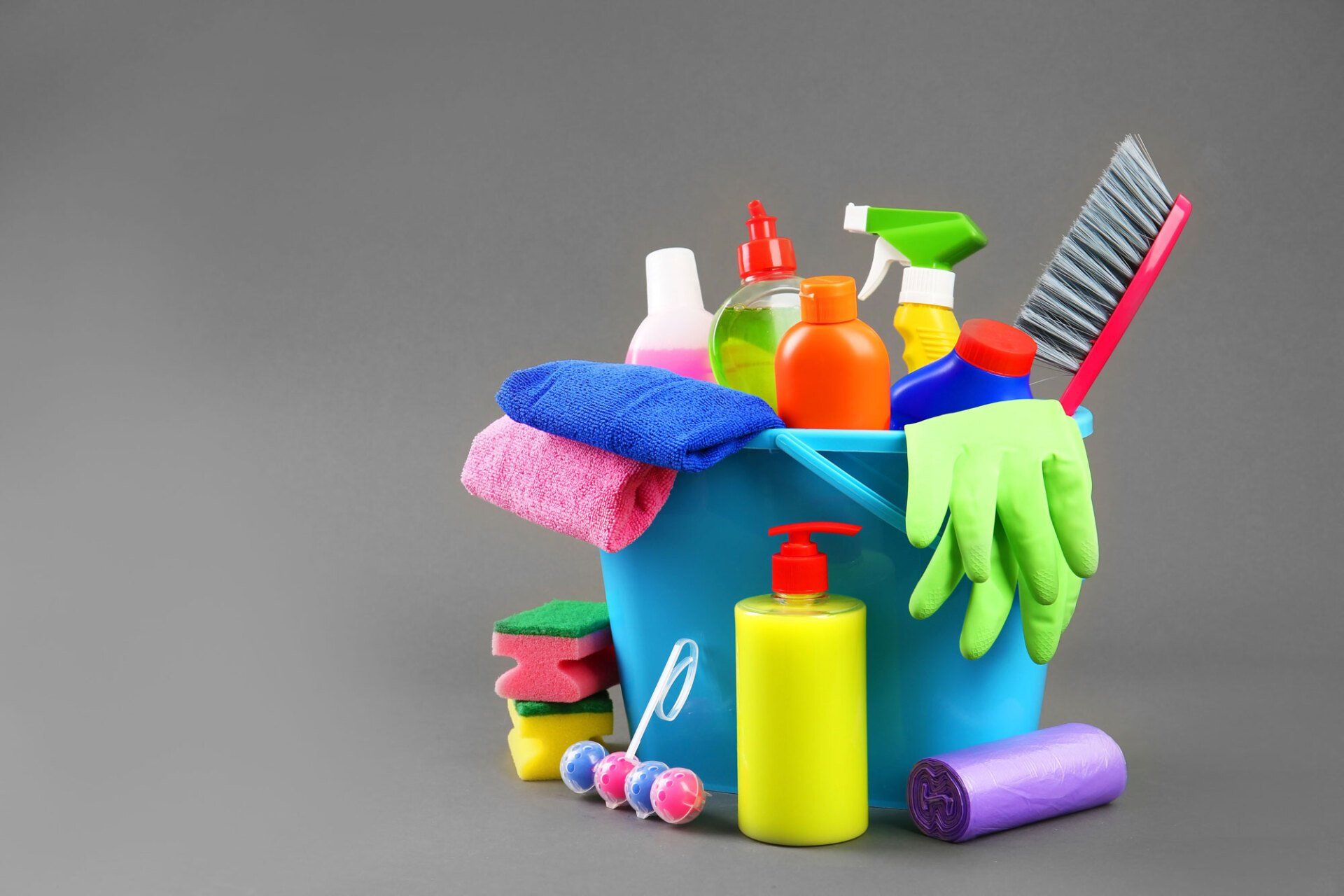 A blue bucket filled with cleaning supplies on a gray background.