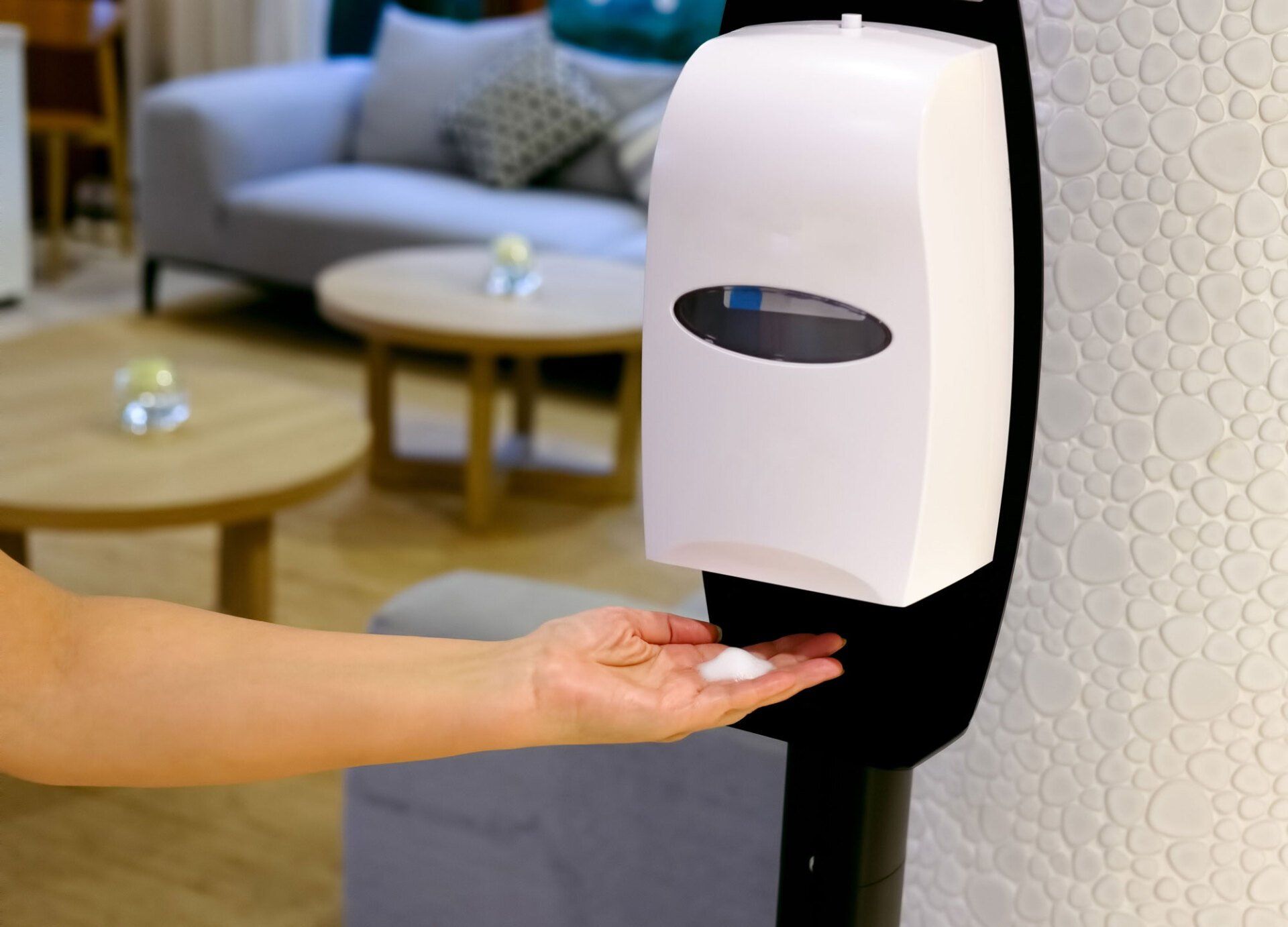 A woman is using a hand sanitizer dispenser in a living room.
