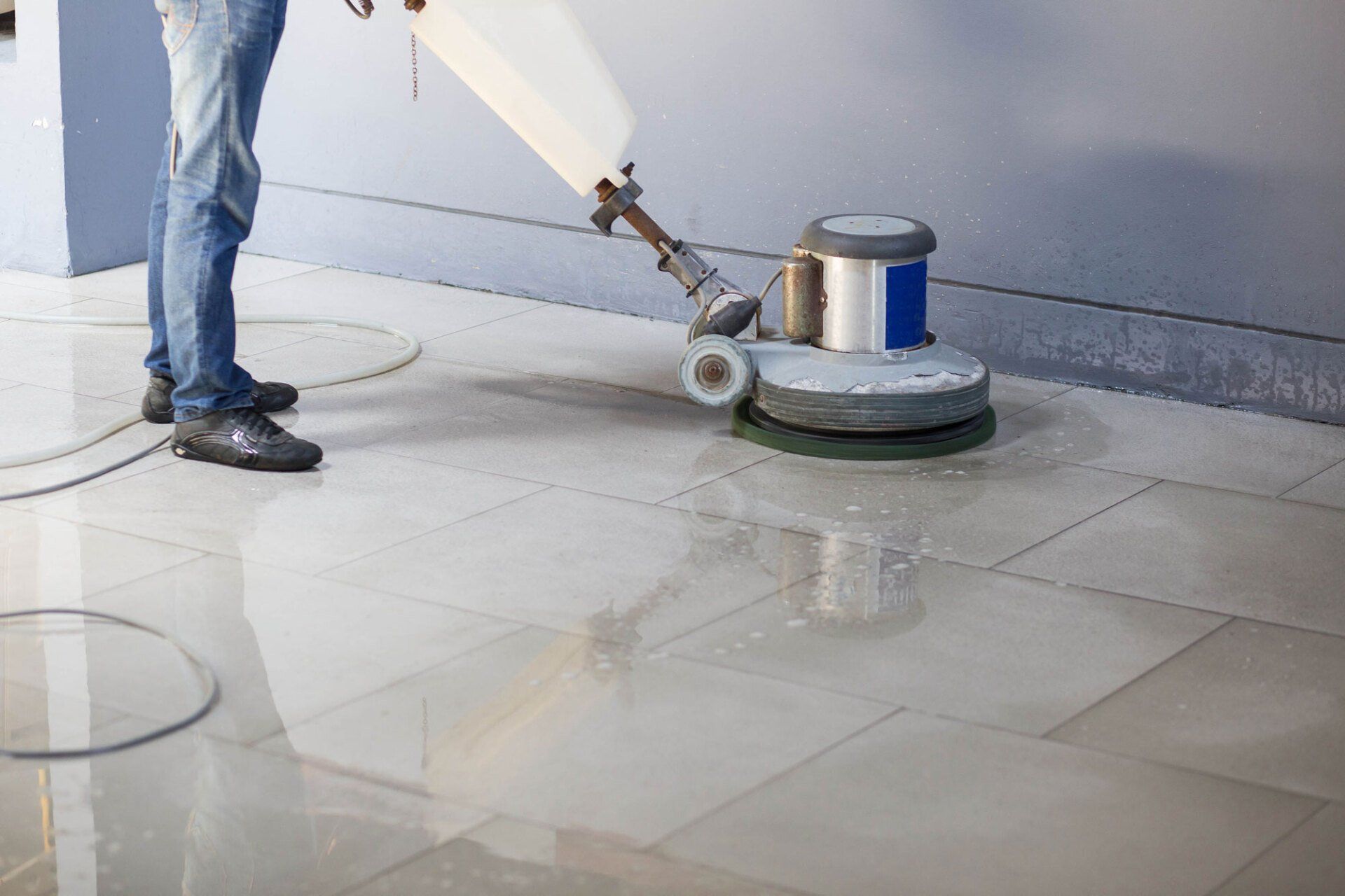 A man is cleaning a tiled floor with a machine.