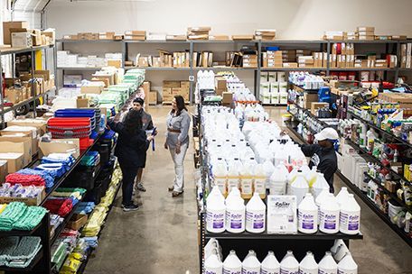 Warehouse interior with shelves stocked with cleaning supplies and boxes; people browsing.