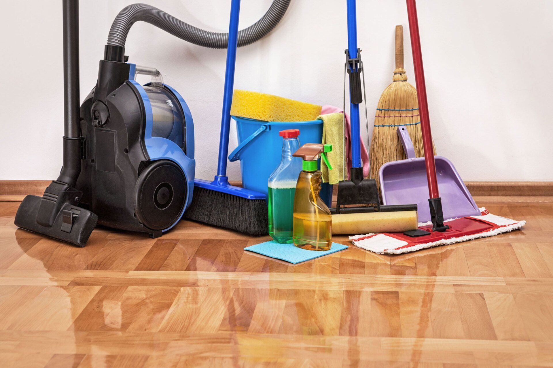 A vacuum cleaner and cleaning supplies are on a wooden floor.