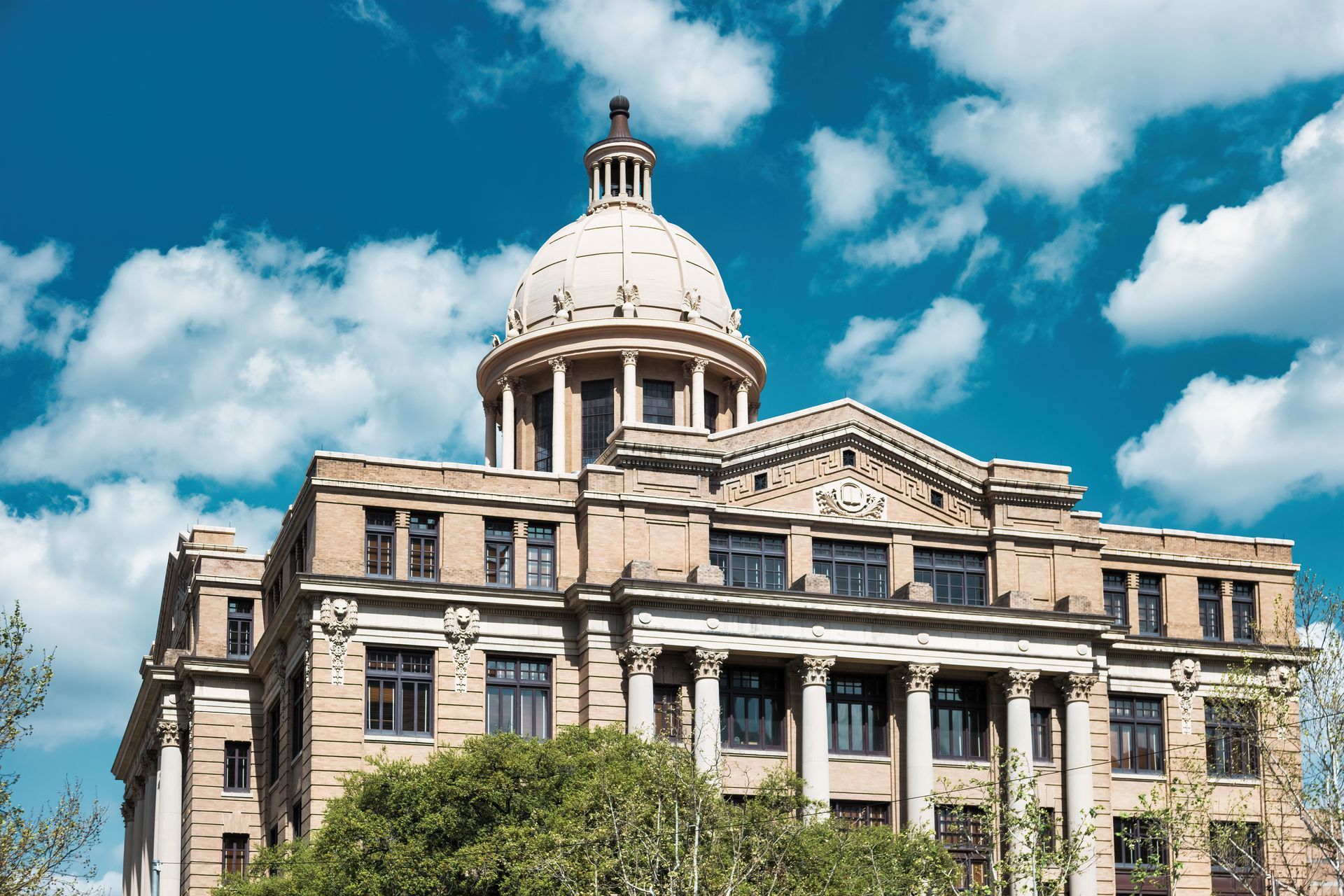 Beige courthouse with a dome, pillars, and multiple windows against a blue sky with clouds.