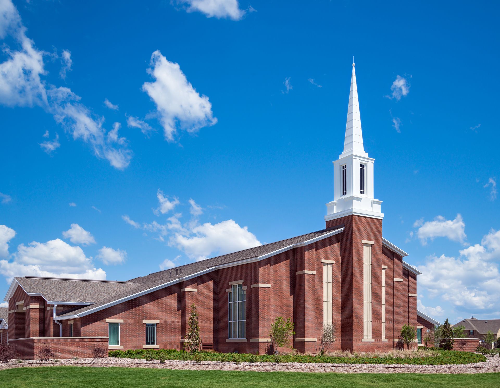 Brick church with white steeple against a blue sky, green grass in front.