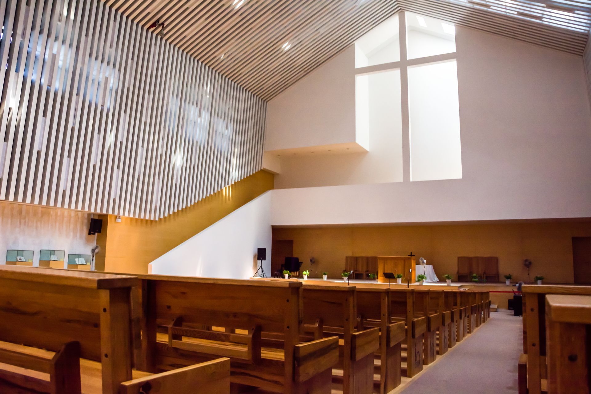 Interior view of a modern church with wooden pews, a large cross-shaped window, and a sloped ceiling.