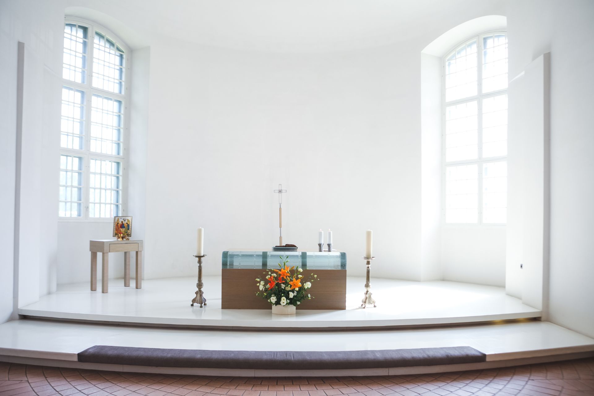White chapel interior with altar, flowers, candles, and arched windows.