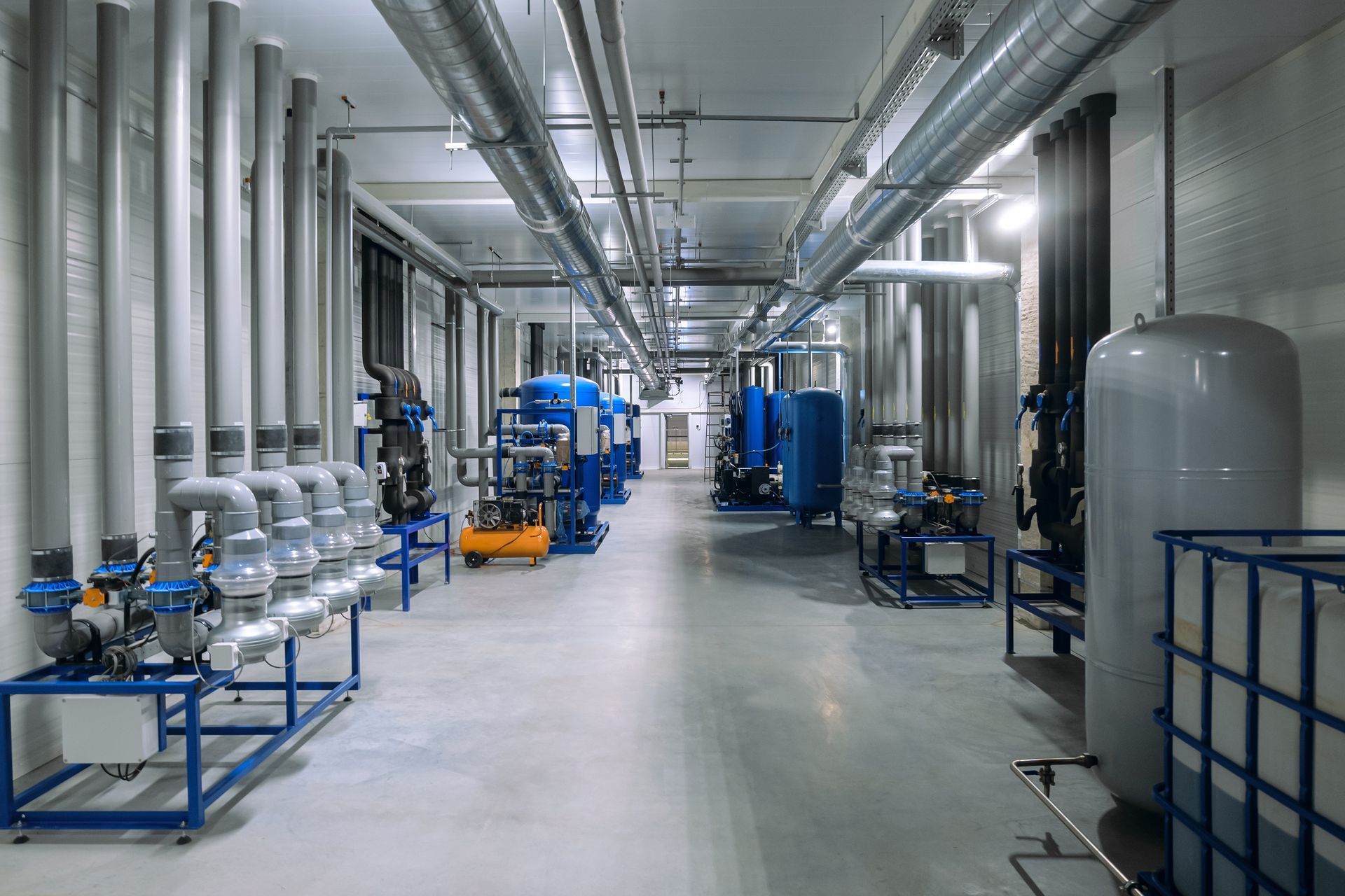 Industrial hallway with pipes, tanks, and machinery; light gray walls and floor.