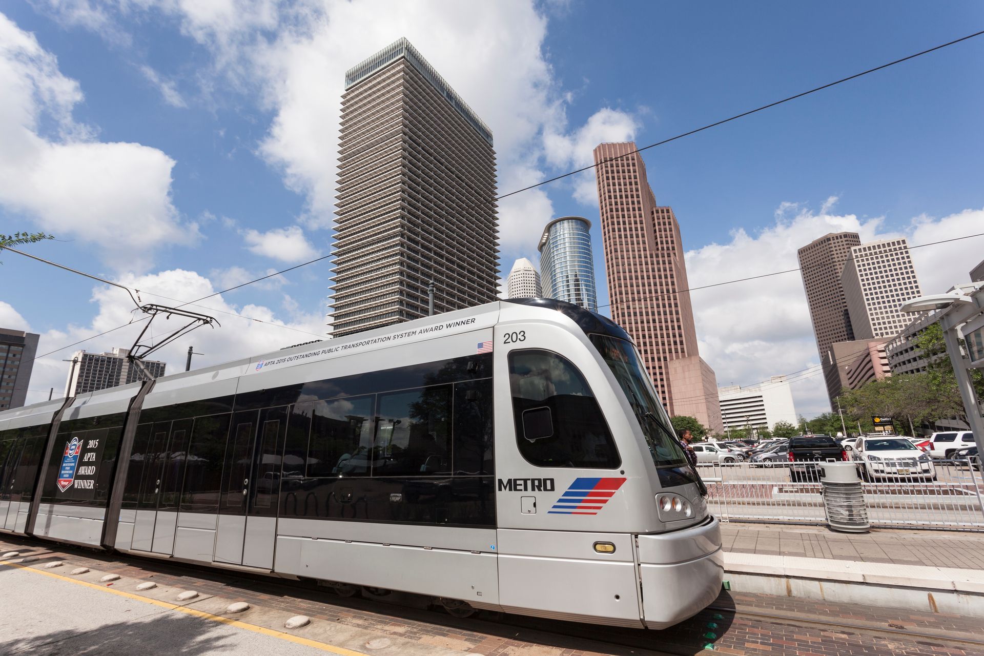 Light rail train in Houston, TX, with skyscrapers in the background on a sunny day.