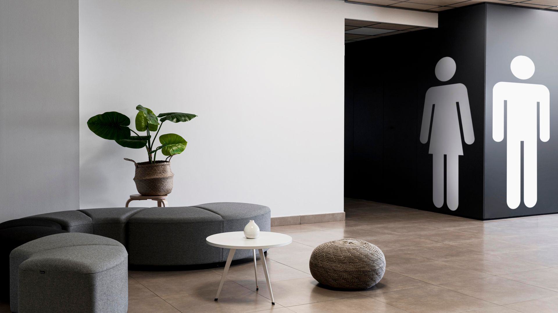 Waiting area with seating, potted plant, and restroom signs on black wall.