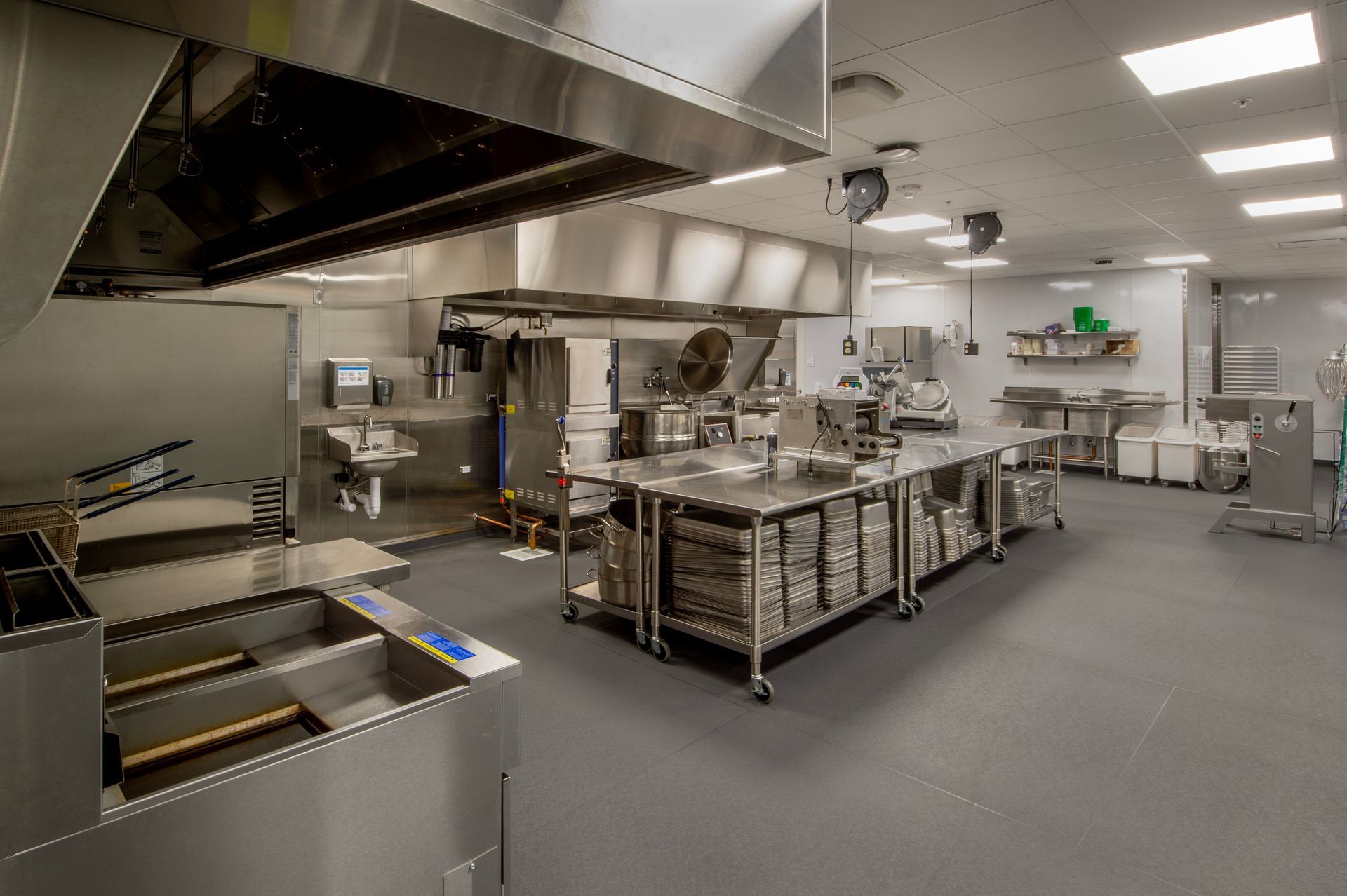 Commercial kitchen interior with stainless steel equipment and a large vent hood.